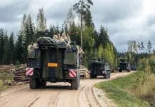 Колона військових бронемашин рухається ґрунтовою дорогою через ліс під час військових навчань