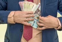 The Rada refused to cap civil servants’ salaries at 80,000 A man in a business suit is holding bundles of Ukrainian hryvnias tucked into his jacket, illustrating the issue of high salaries for officials and budgetary constraints.