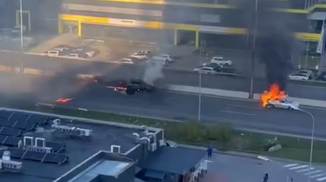 Two cars are on fire on the carriageway, with thick black smoke rising above them following a suspected drone attack.