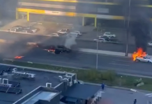 Two cars are on fire on the carriageway, with thick black smoke rising above them following a suspected drone attack.