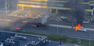 Two cars are on fire on the carriageway, with thick black smoke rising above them following a suspected drone attack.