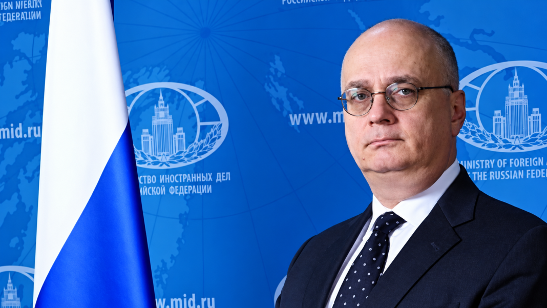 Російський дипломат Гліб Десятников у діловому костюмі на тлі символіки Міністерства закордонних справ Росії та державного прапора РФ