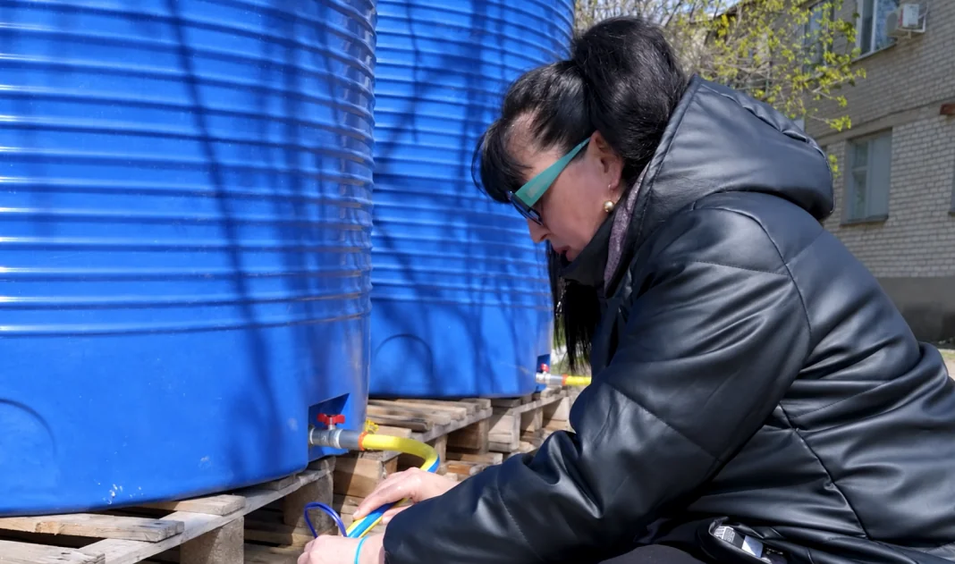 Новояворівськ без води Жінка набирає воду зі спеціальної ємності через шланг біля великих синіх резервуарів для питної води.