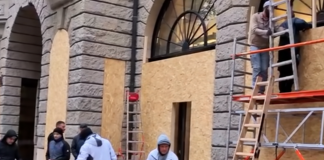 Workers are fitting wooden panels to the windows and shop fronts of a shop in Germany.