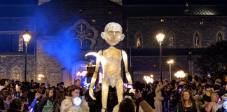 A giant illuminated puppet amongst the crowd of spectators at a night-time Halloween parade in Ireland